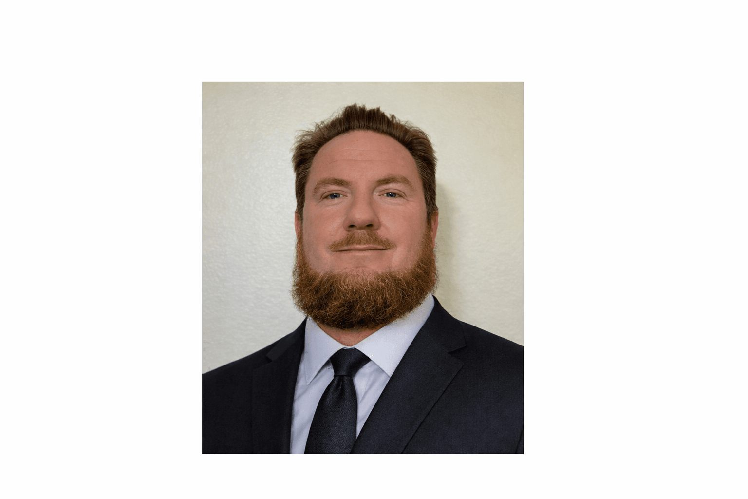 Professional headshot of a man with a reddish-brown beard wearing a dark suit and tie.