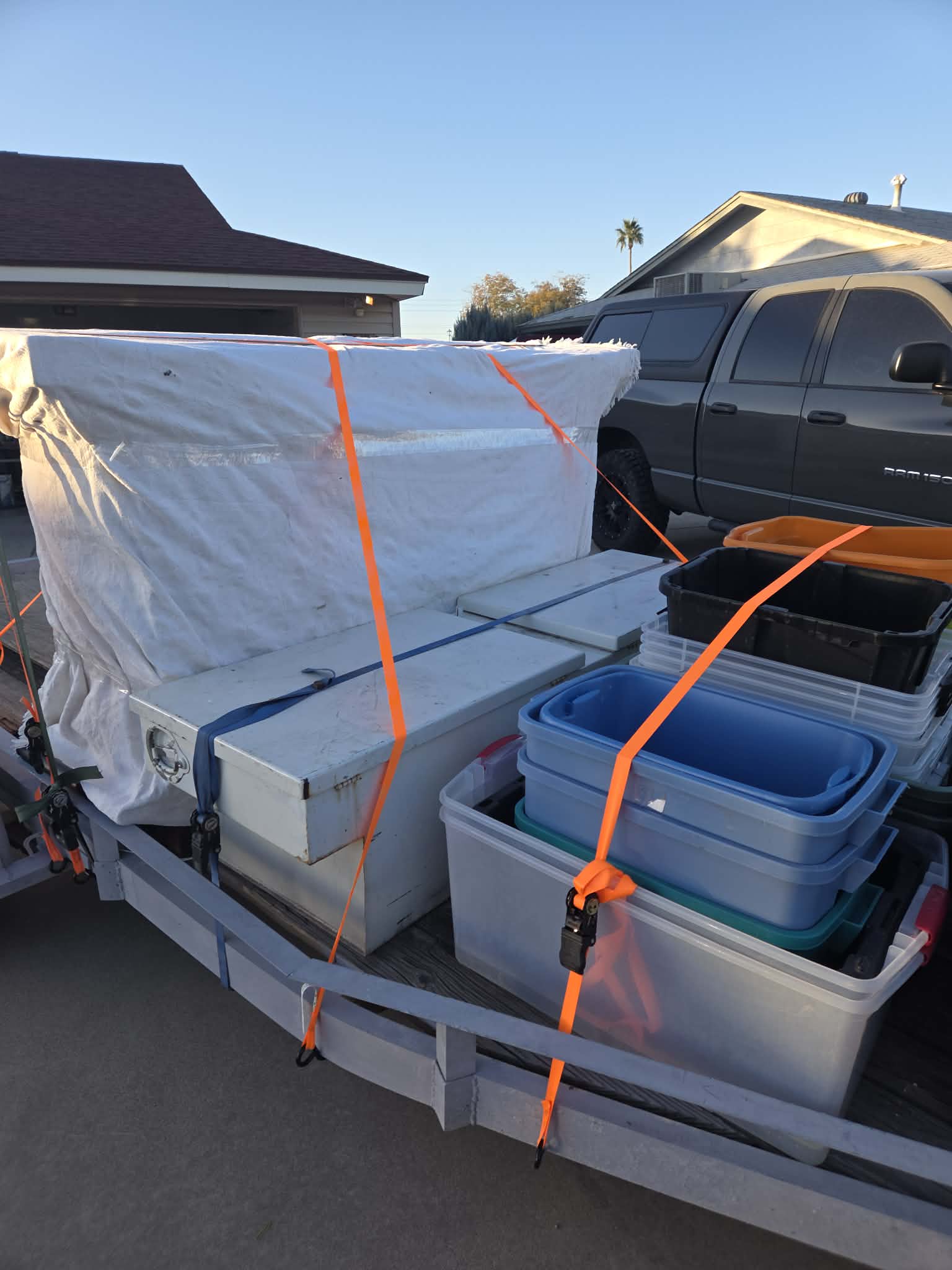 Storage bins and a large tarp-covered object secured to a trailer with orange ratchet straps.